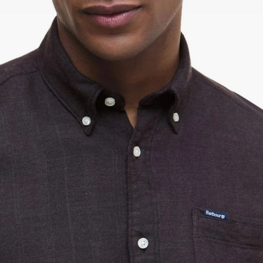 Close-up of a person wearing a dark brown button-up shirt with a visible brand logo.