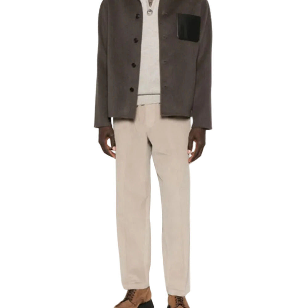 Person wearing a dark jacket, light shirt, beige pants, and brown shoes on a white background