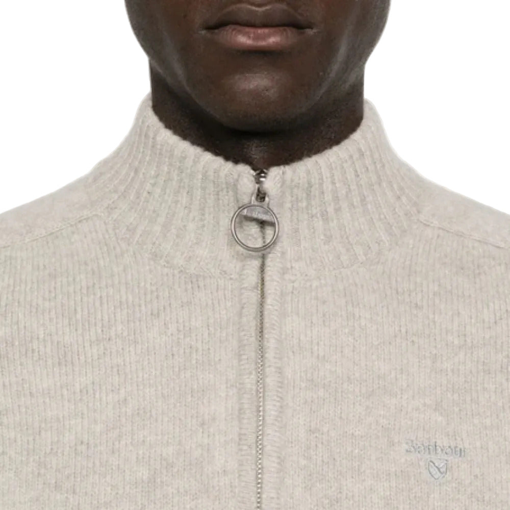 Close-up of a person wearing a beige zip-up sweater with a neutral background