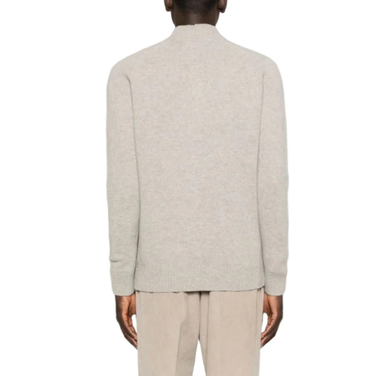 Person wearing a light gray sweater and beige pants on a white background