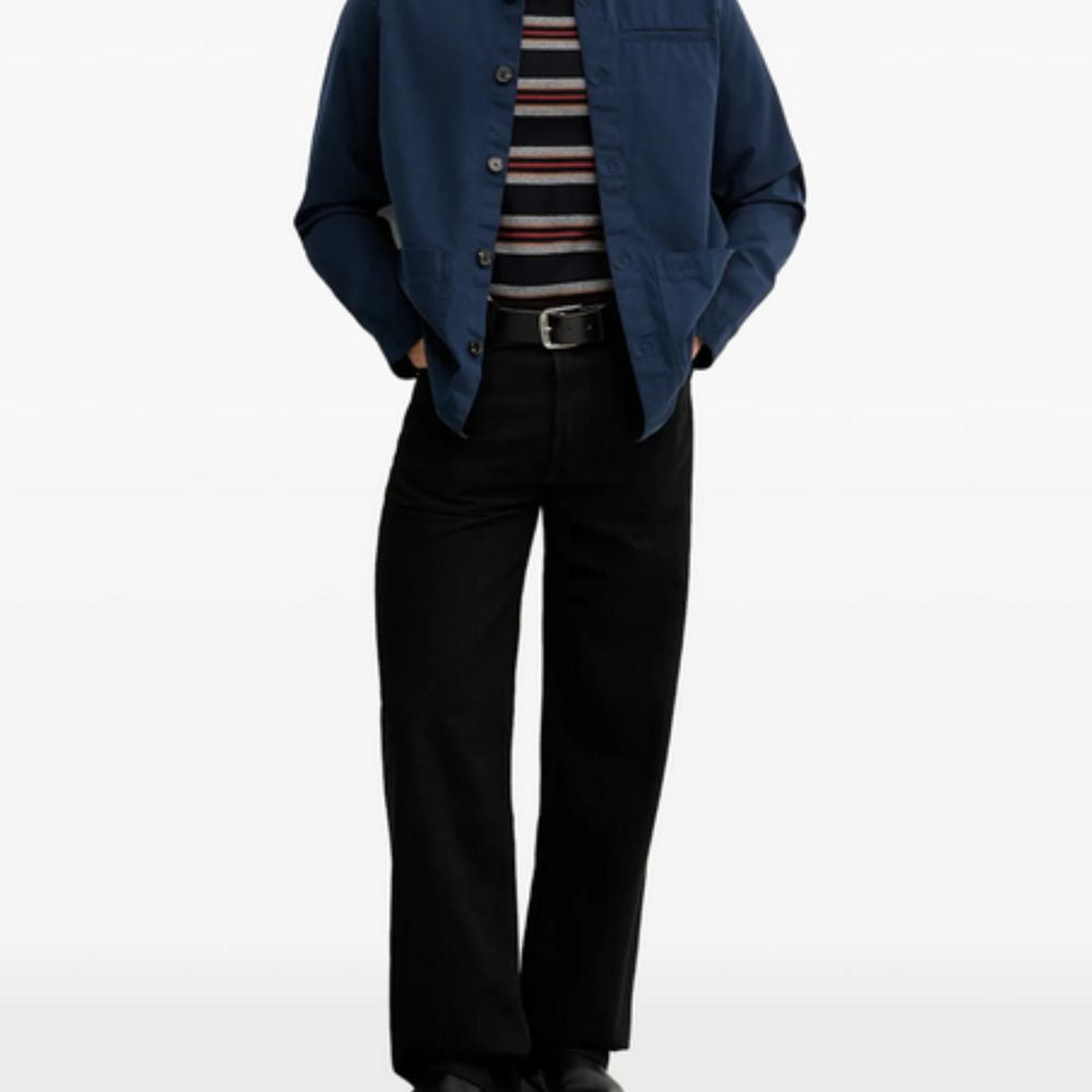 Person wearing a blue shirt over a striped sweater with black pants on a white background