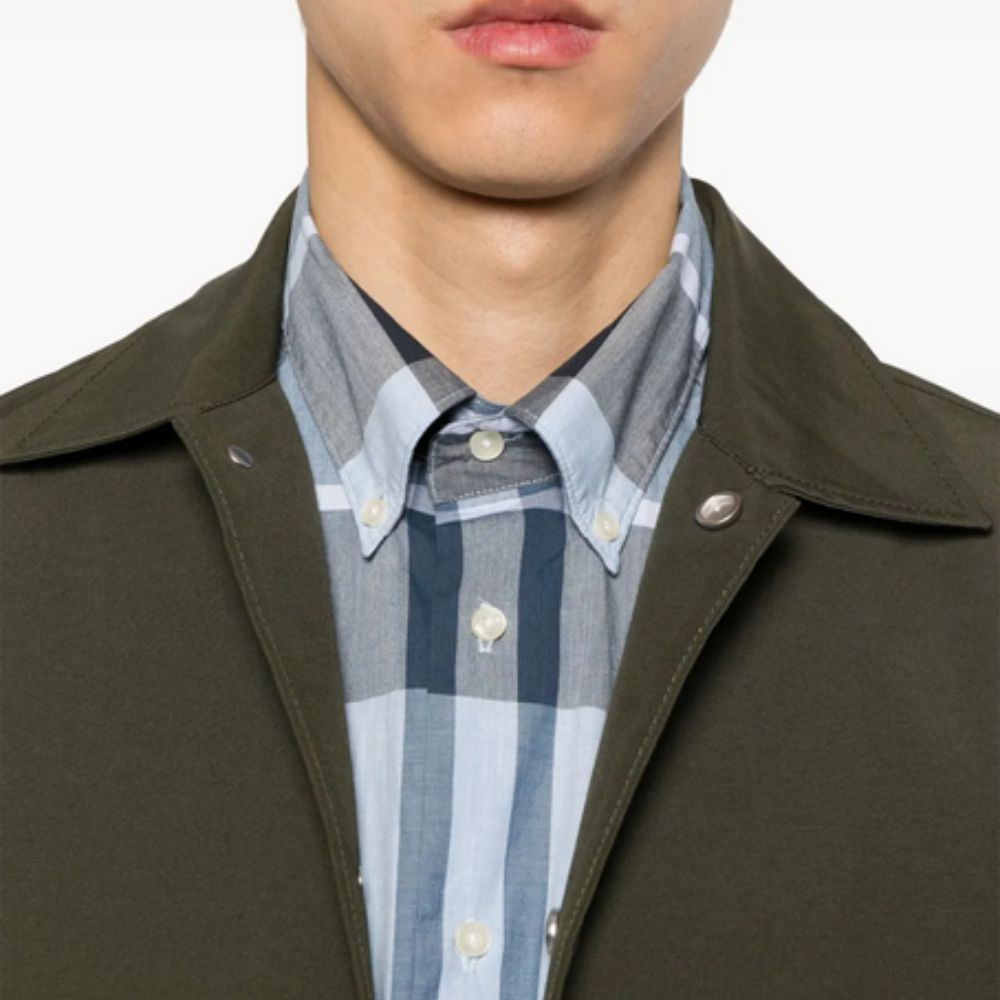Close-up of a person wearing a dark green coat over a plaid shirt with a blurred background