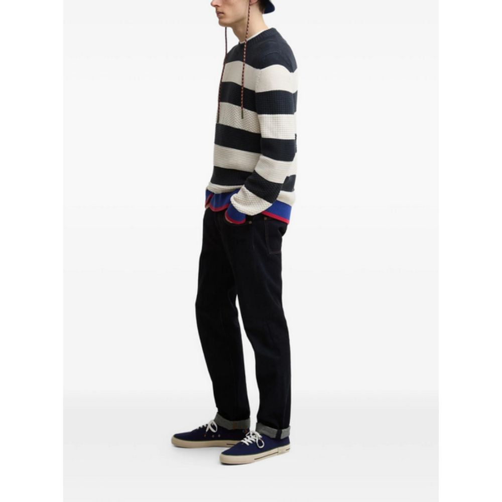 Person wearing a black and white striped sweater with colorful cuffs and hem on a white background