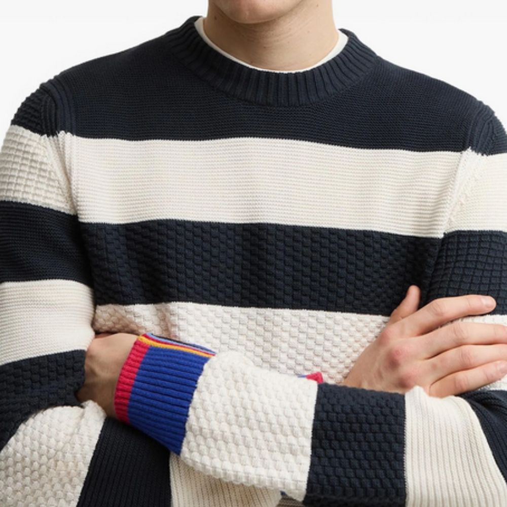 Person wearing a navy and white striped BARBOUR X PAUL SMITH Relaxed Nautical-Style Sweater with colorful cuffs.