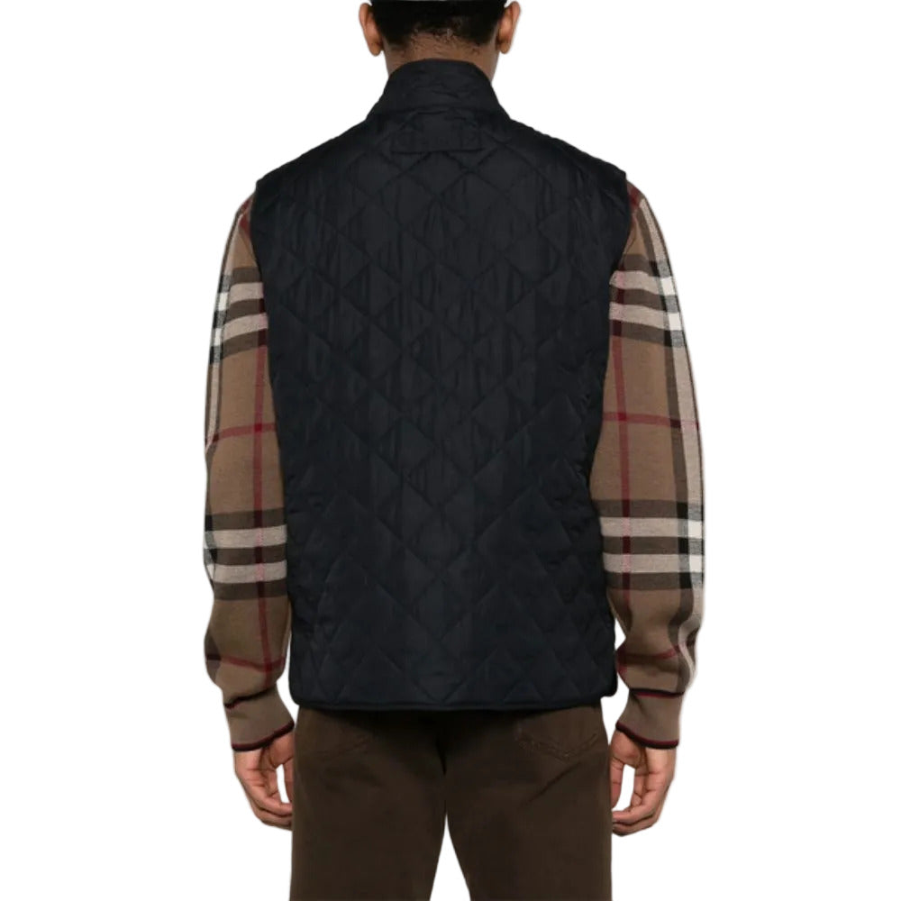 Person wearing a black quilted vest over a plaid shirt on a white background