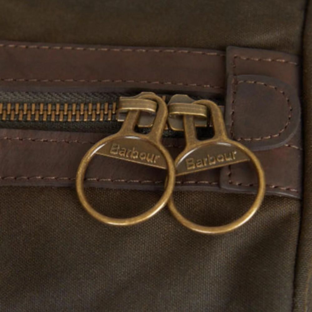 Close-up of a brown leather bag with gold zipper pulls featuring the Barbour logo.