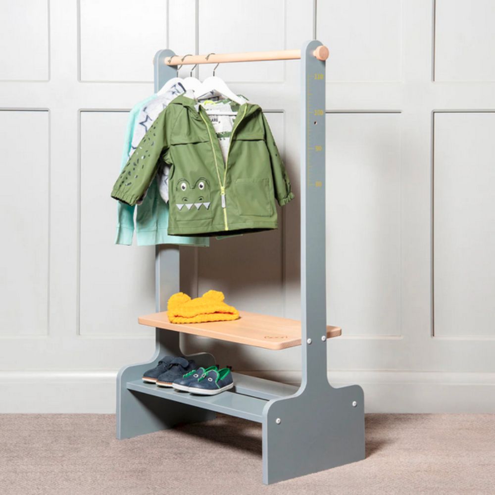 Children's coat rack with green jacket, yellow shoes, and blue shoes against a white paneled wall.