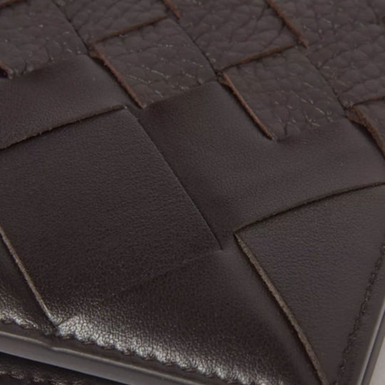 A close-up shot of a brown Bottega Veneta bi-fold wallet, showcasing the signature intrecciato (woven) calf leather texture and stitching detail.