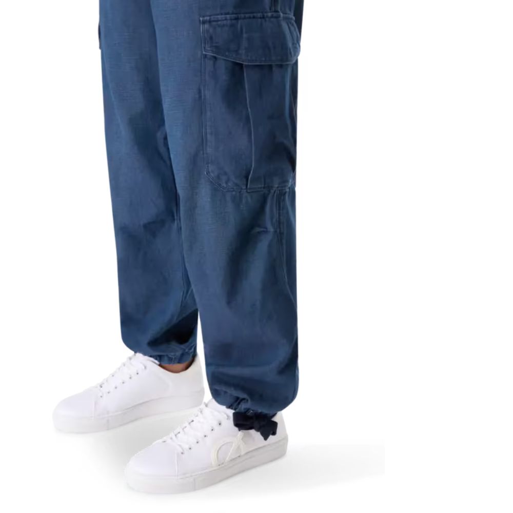 A close-up of a person's legs wearing dark blue cargo pants with large pockets on each leg. The pants have a cuffed bottom and are paired with white sneakers.