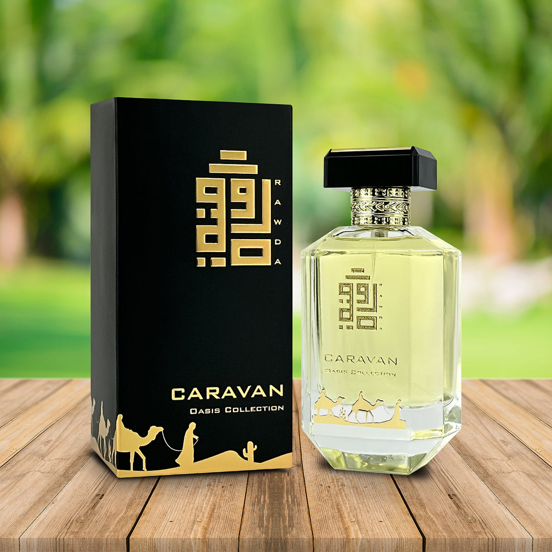 An EDP 100mL bottle of Caravan fragrance by Rawda along with its Box kept on a wooden table with a green garden background