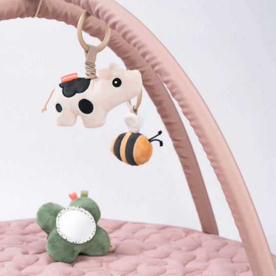 Plush toys including a cow, bee, and frog on a pink play gym with a white background