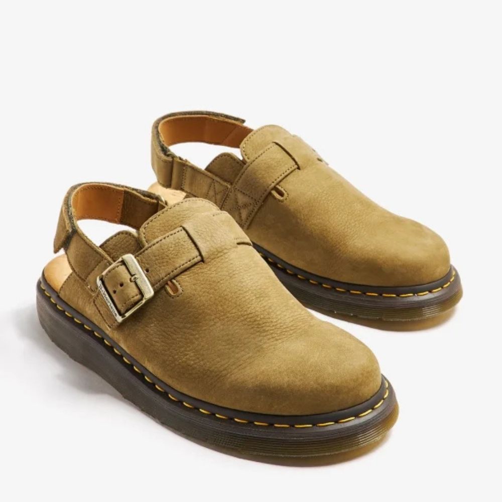 A pair of Dr. Martens Jorge II slingback sandals in brown suede. The sandals feature a chunky rubber sole with yellow stitching, a buckle strap, and a slingback strap