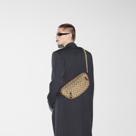 Model wearing the beige crossbody bag with a black trenchcoat and glasses