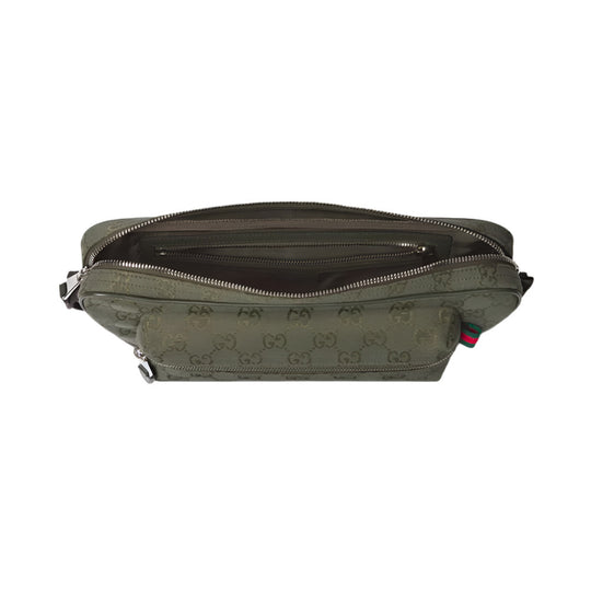 An overhead shot of the GUCCI GG Canvas Large Slingbag, showing the top open. The bag is made of forest green GG canvas with the interlocking GG monogram subtly debossed or printed throughout. The interior is lined with a darker green nylon, and several open pockets and one zippered pocket are visible. On the exterior, near the front, there are two zippered pockets. On the right side, a small tag with the iconic green and red Web detail is visible.
