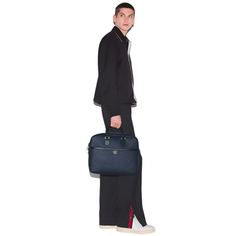 A man in a dark blue jacket and trousers with a red and green stripe holds a dark blue briefcase with a GG logo, against a white background.