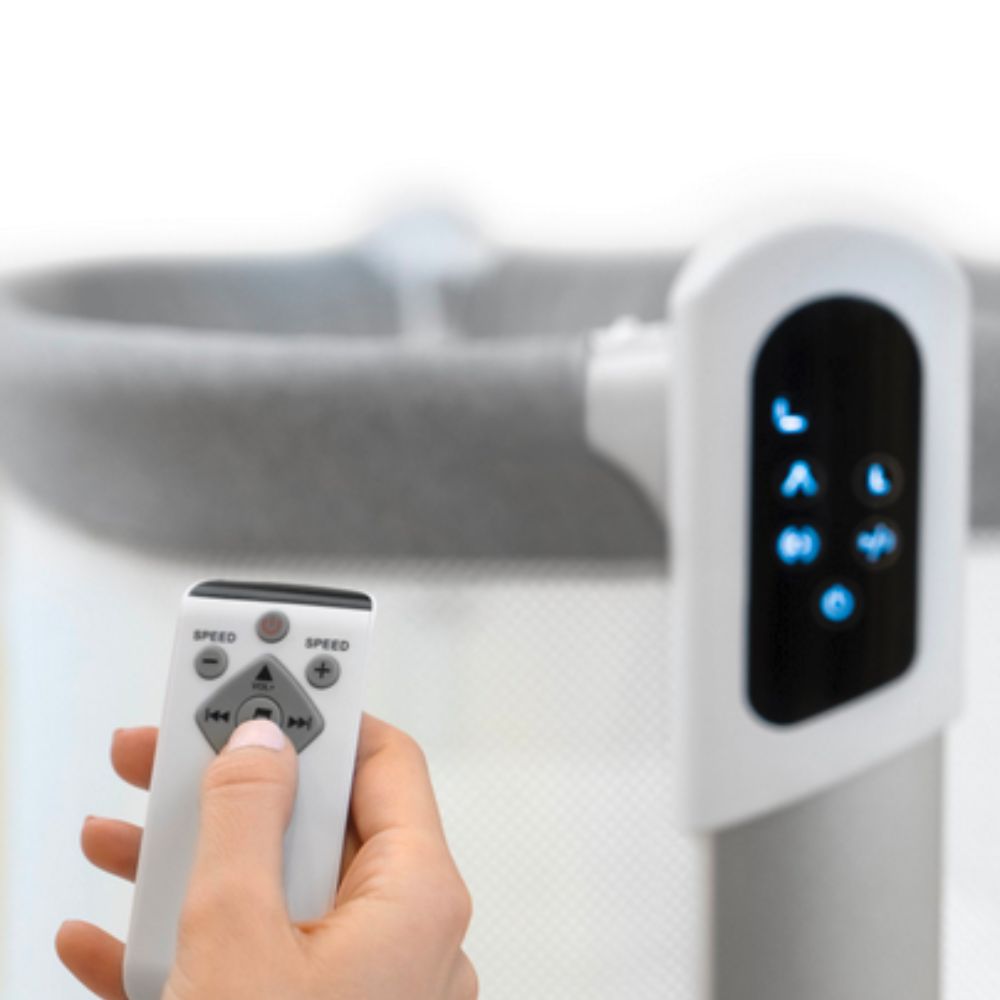 Hand holding a remote control next to a Jikel Pony Portable & Adjustable 2-in-1 Co-Sleeper Bassinet & Electric Baby Swing 
