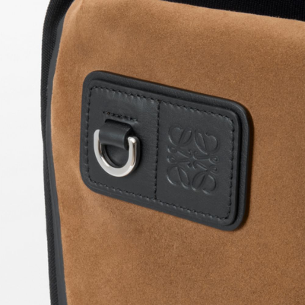 A close-up of a black leather patch on the brown suede of the LOEWE Flex Roll-Top Backpack