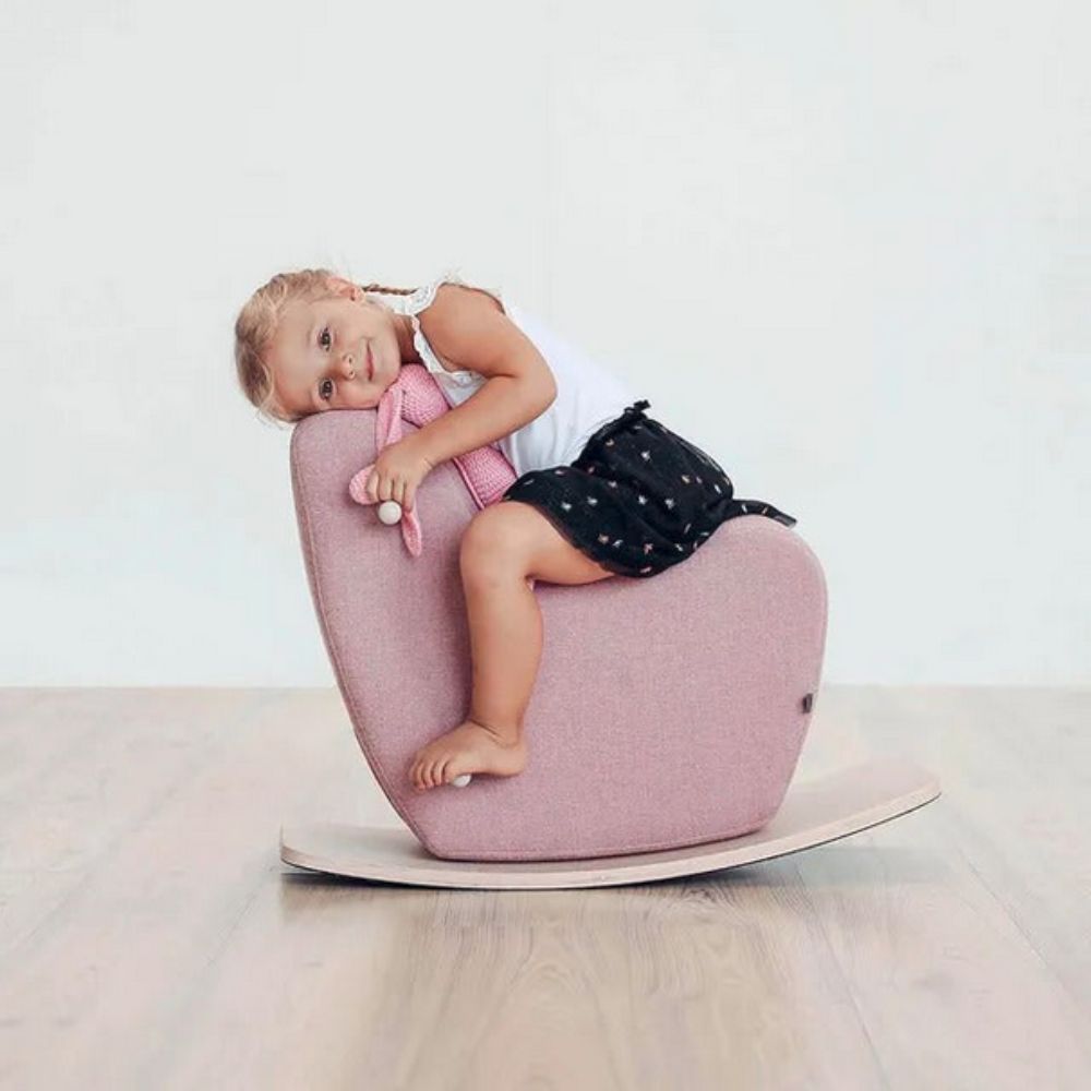Child sitting on a Momcozy Sturdy Safe Pale Pink Rocking Horse against a white background