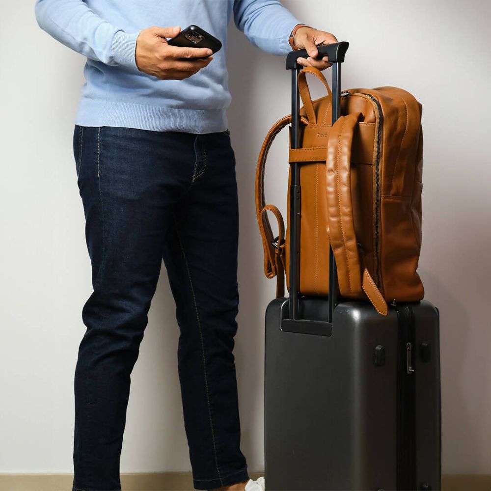Person holding a phone next to a black suitcase and brown leather backpack against a plain background