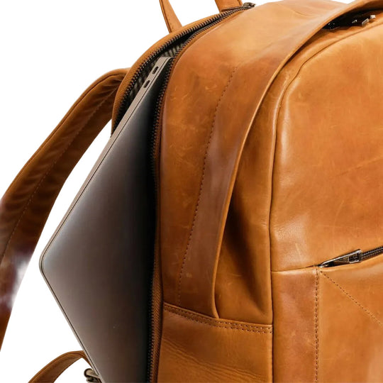 Brown leather backpack with a laptop inside on a light gray background