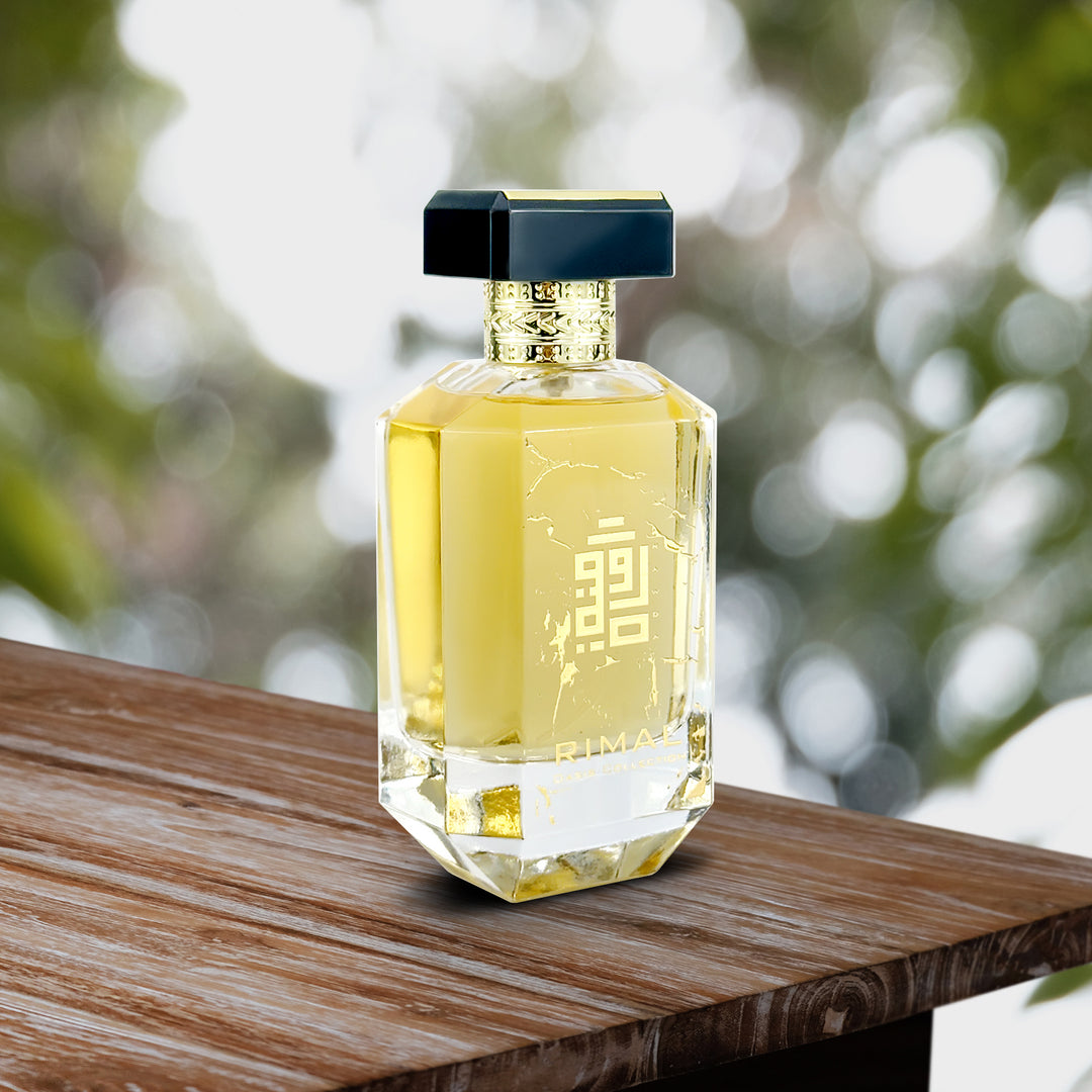 An EDP 100mL bottle of Rimal perfume by Rawda kept on a wooden table against a green garden backdrop