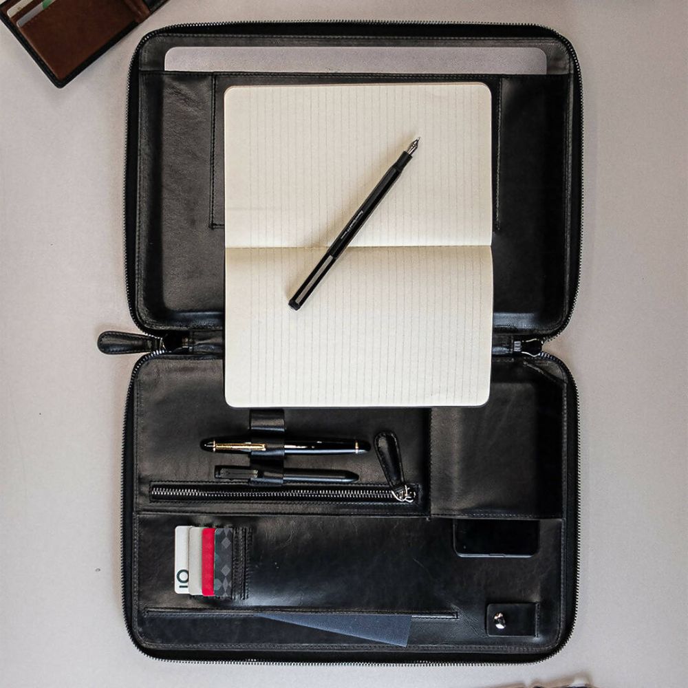 Black leather briefcase with a notebook, pen, and card holder on a light gray background