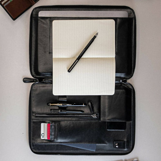 Black leather briefcase with a notebook, pen, and card holder on a light gray background