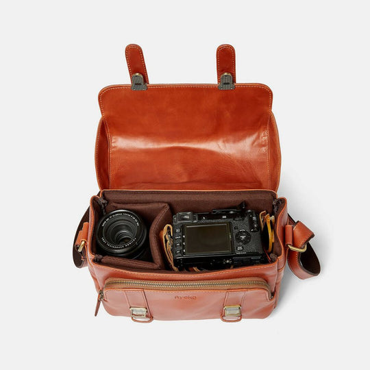 Brown leather camera bag with a camera and lens inside on a white background