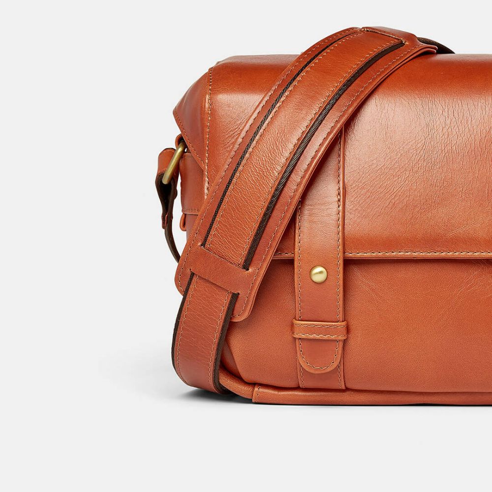 Brown leather bag with a strap on a light gray background