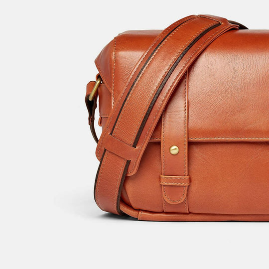 Brown leather bag with a strap on a light gray background