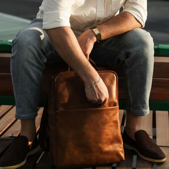 Person sitting on a bench with a brown leather bag