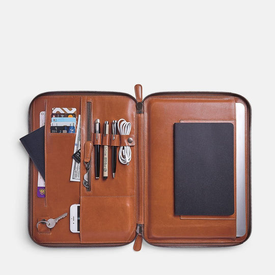 Caramel leather organizer with various items on a light gray background