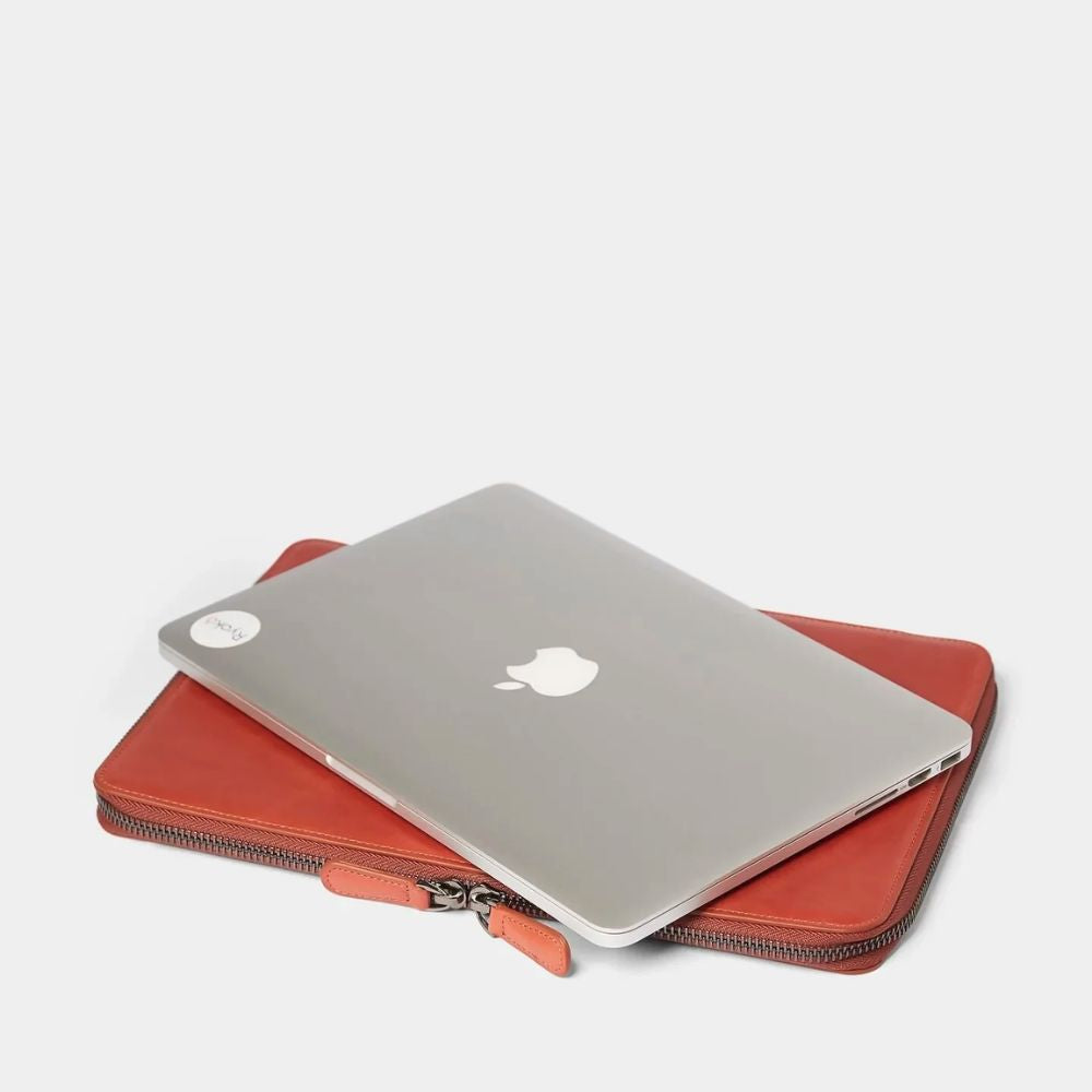 Silver laptop with Apple logo on a tan colored case on a white background