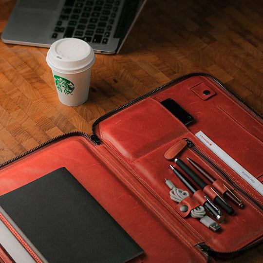Red leather case with tools, a Starbucks cup, and a laptop on a wooden surface