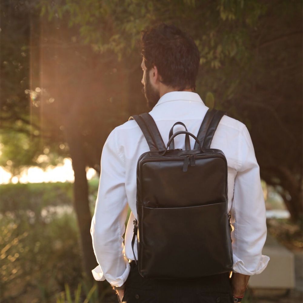 Man wearing a black backpack walking outdoors with trees in the background