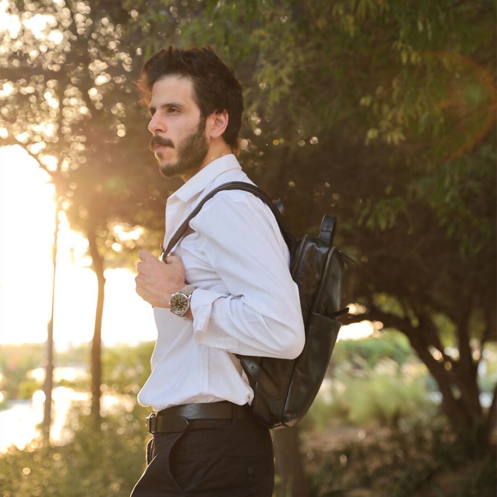 Man with a backpack standing outdoors with trees and sunlight in the background