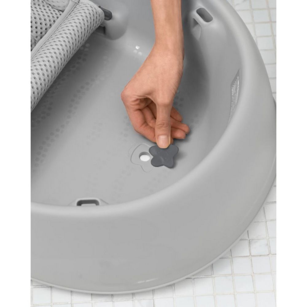 Gray bath seat with a hand placing a star-shaped object inside on a tiled floor.