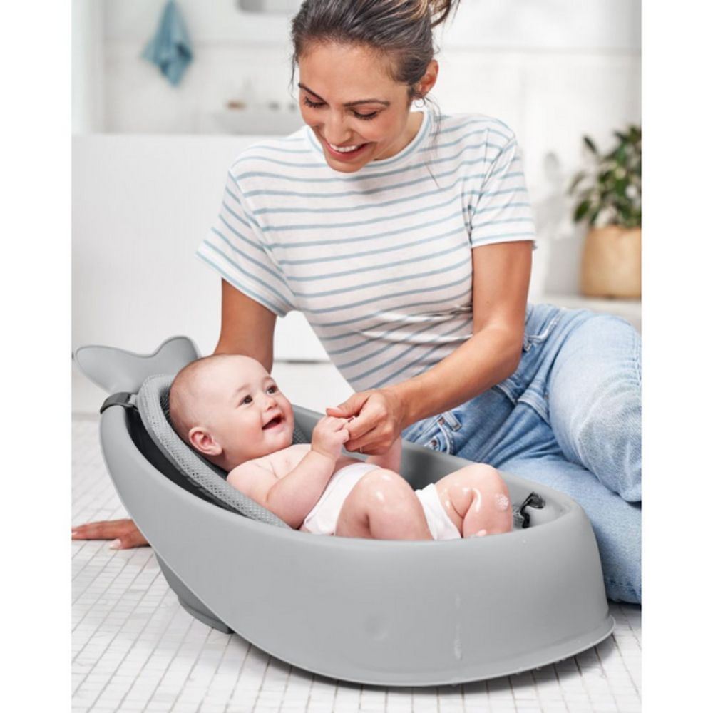 Woman sitting on the floor with a baby in a gray baby seat, smiling.