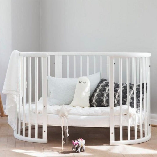 Stokke Sleepi Bed White with pillows and a toy in a room with a light gray wall.