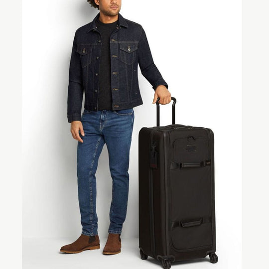 Man in denim jacket and jeans holding a black suitcase on a white background