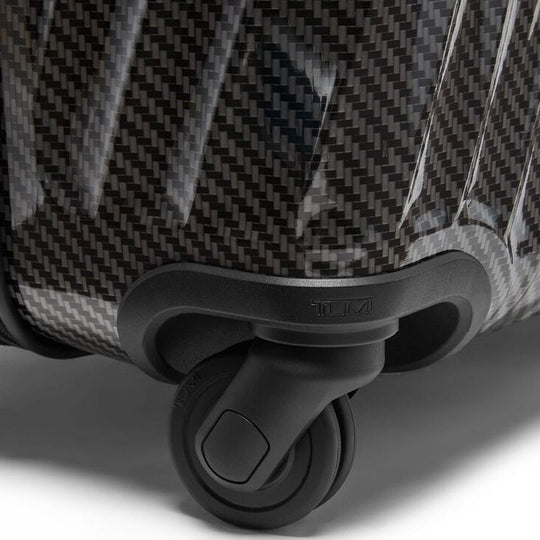 Close-up of a suitcase with a textured surface and black wheel on a light background