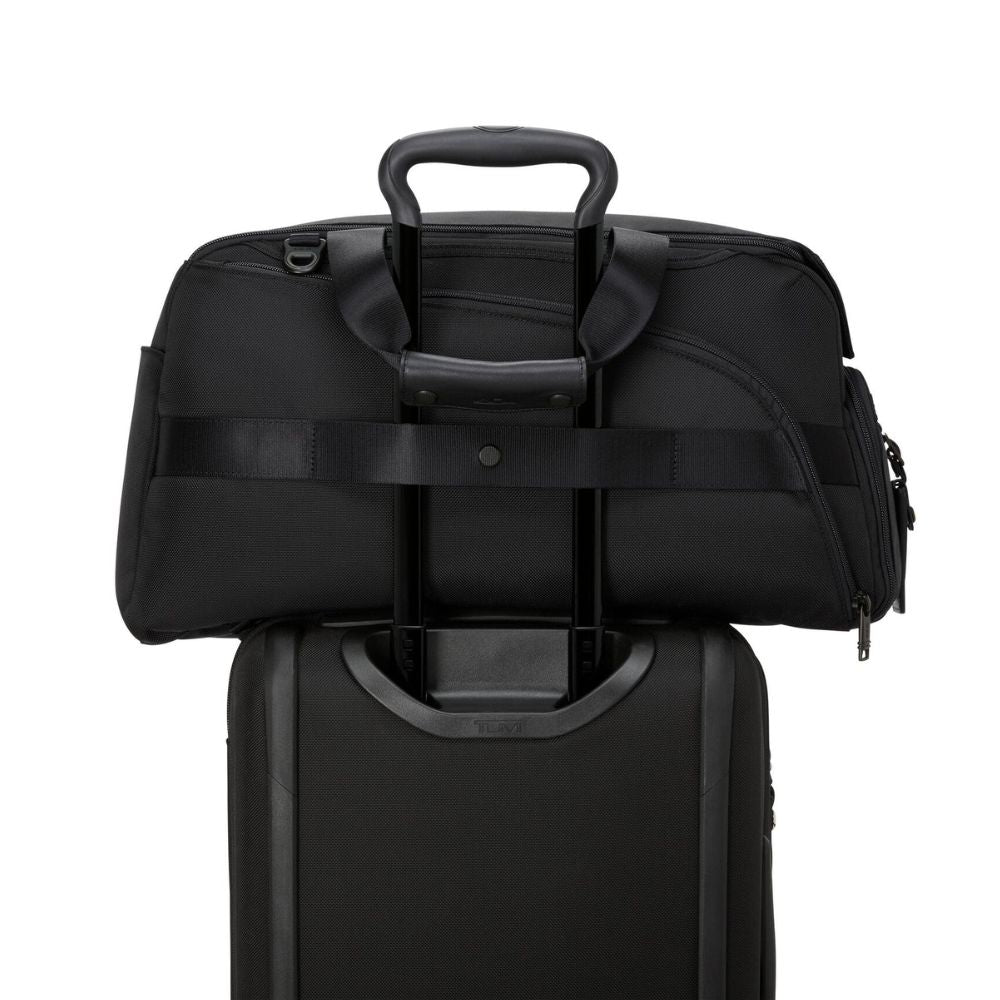 Black duffel bag stacked on top of a suitcase on a white background