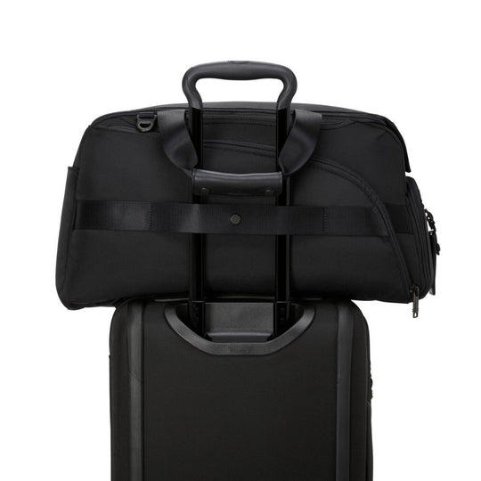Black duffel bag stacked on top of a suitcase on a white background