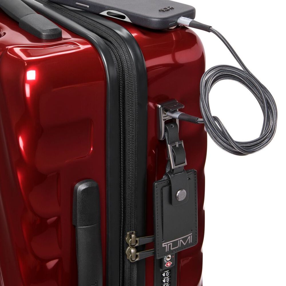 Red suitcase with a black handle and Tumi luggage tag, featuring a security cable.