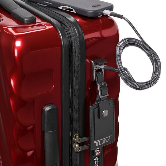 Red suitcase with a black handle and Tumi luggage tag, featuring a security cable.
