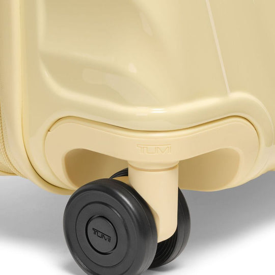 Close-up of a beige TUMI suitcase with a black wheel on a light gray background