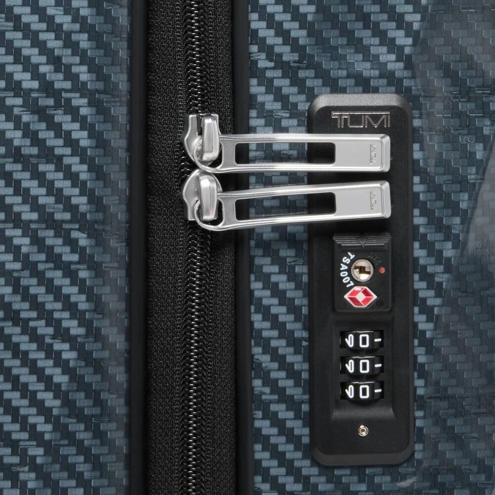 Close-up of a TUMI suitcase with a zipper and combination lock on a textured surface.