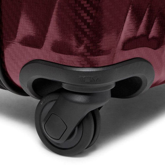 Close-up of a suitcase wheel on a red suitcase with 'TUMI' branding.