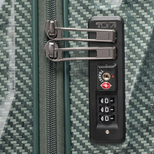 Close-up of a TUMI suitcase with a combination lock on a textured green surface