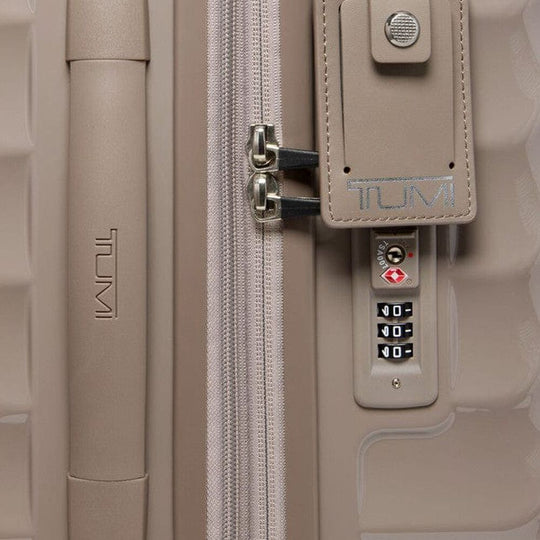 Close-up of a beige Tumi suitcase with a combination lock.